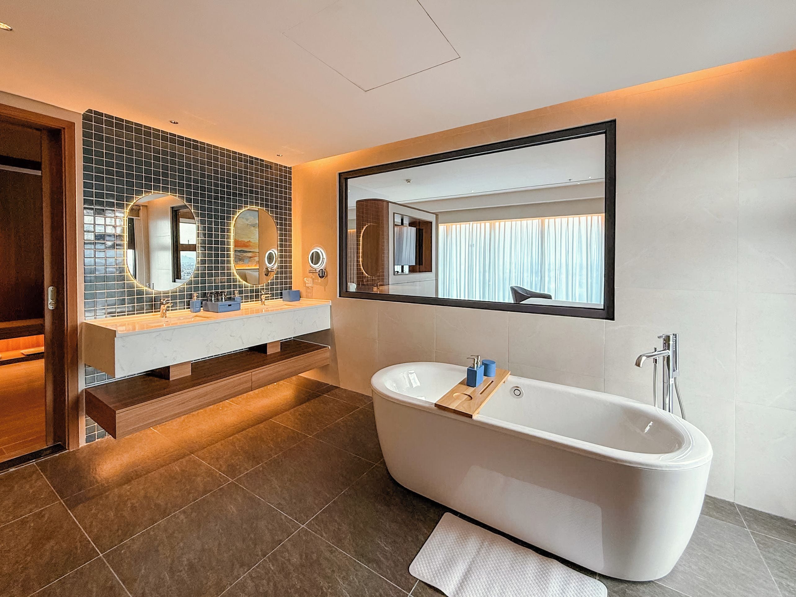 A modern bathroom with a freestanding bathtub, a large mirror, and a vanity with two sinks.