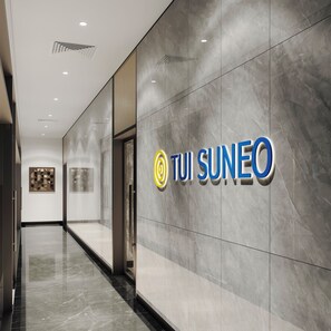 A modern hallway with a TUI SUNEO sign, marble walls, and a glass door.