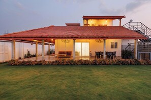 A two-story house with a red-tiled roof, a covered patio area with seating, and a well-maintained lawn.