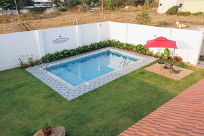 A rectangular swimming pool with a tiled border, surrounded by a white wall and a small grassy area.