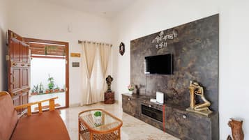 A living room with a sofa, a glass coffee table, a flat-screen TV mounted on a marble wall, and a decorative statue.