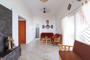 A spacious living room with a marble floor, a red sofa, wicker chairs, and a coffee table.