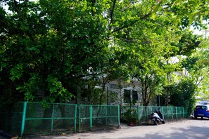 Ein von einer Hecke umgebenes Grundstück mit Bäumen, einem Elektroroller und einem Gebäude im Hintergrund.