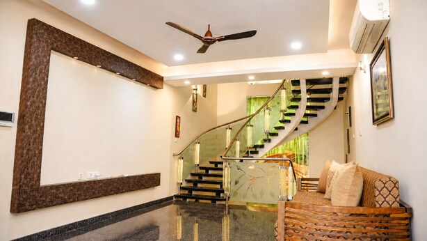 A modern interior with a curved staircase, a ceiling fan, and a seating area with patterned cushions. - Cherryblossom by Redolive3bhkecr Beachesit Park (Tirupporur)