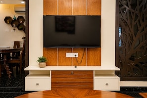 A modern living room with a flat-screen TV mounted on a wooden panel wall, a white console table with drawers, and a decorative plant.