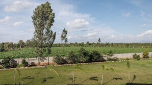 A view of a landscaped area with a grassy field, trees, and a distant mountain range. - Crystal Blue Villa by Stayjadeprivatepoolvegfood (Doddaballapur)