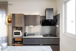 A compact kitchen with a microwave, gas stove, and a small refrigerator. - Crystal Blue Villa by Stayjadeprivatepoolvegfood (Doddaballapur)