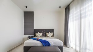 A modern bedroom with a bed, bedside tables, a bench, and a large window with curtains. - Crystal Blue Villa by Stayjadeprivatepoolvegfood (Doddaballapur)