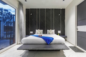 Une chambre moderne avec un grand lit, des tables de chevet et une vue sur l’extérieur grâce à une porte coulissante.