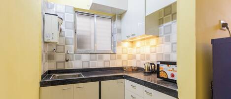 A compact kitchen with white cabinets, a black countertop, and a window with a frosted glass.