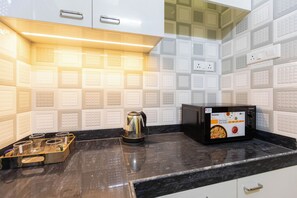 A kitchen with white tiled backsplash, a black countertop, a coffee maker, and a microwave. - City Haven by Jadecaps 3bhk South Kolkata (Kolkata)