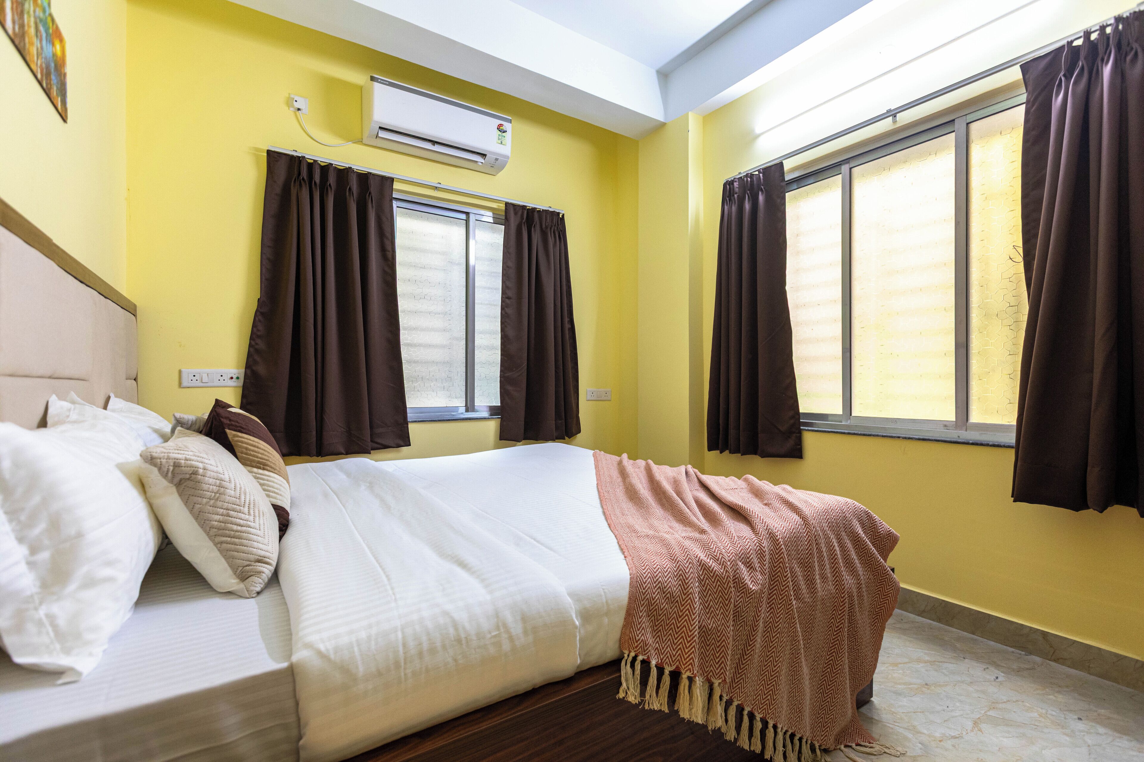 A hotel room with a bed, curtains, an air conditioning unit, and a window.