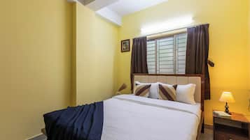 A bedroom with a bed, a nightstand, a lamp, a window with curtains, and a picture on the wall.