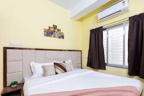 A neatly made bed with a headboard, a window with curtains, and a wall-mounted air conditioner. - City Haven by Jadecaps 3bhk South Kolkata (Kolkata)