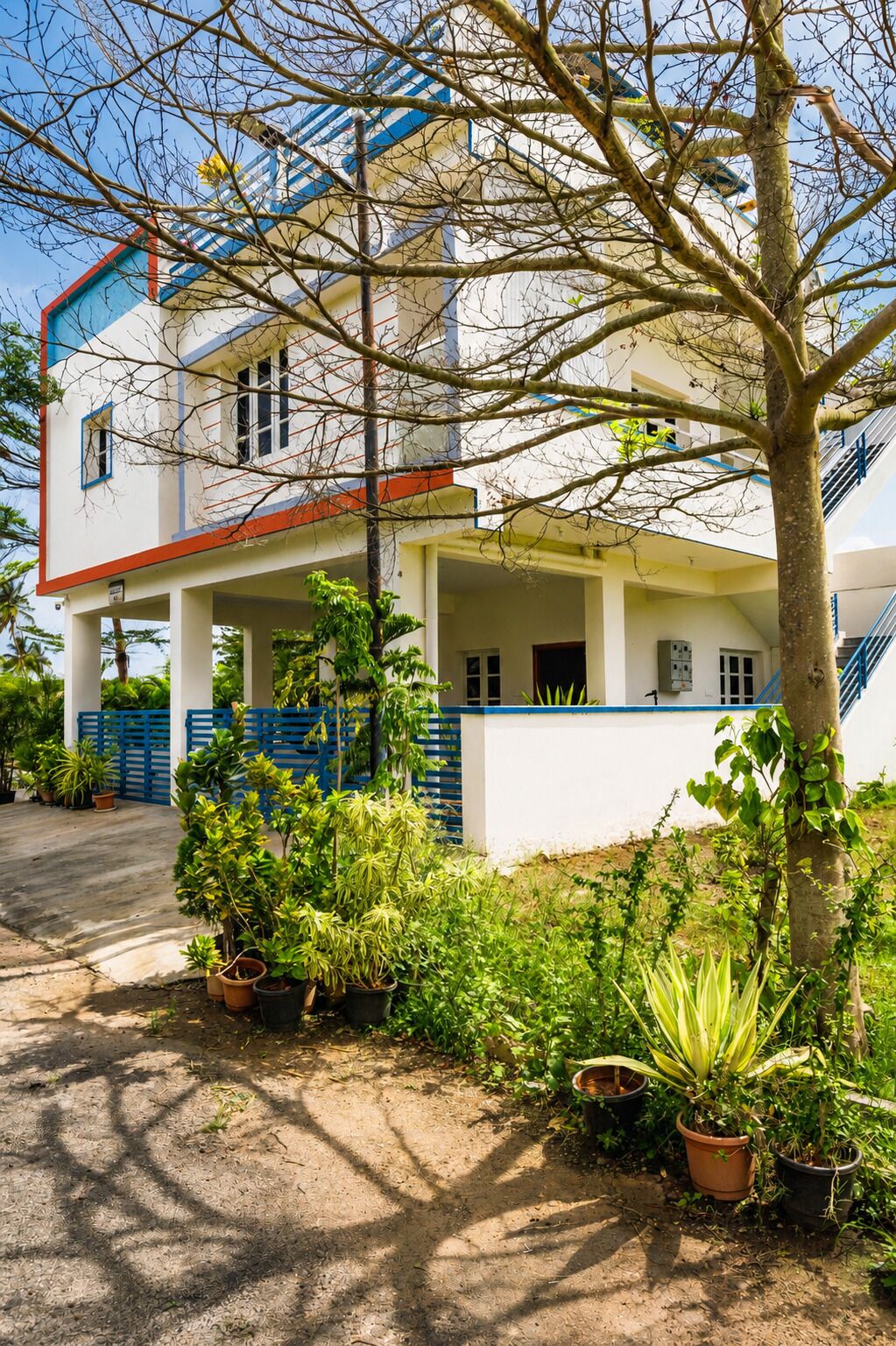 A two-story building with a covered porch, potted plants, and a blue fence.