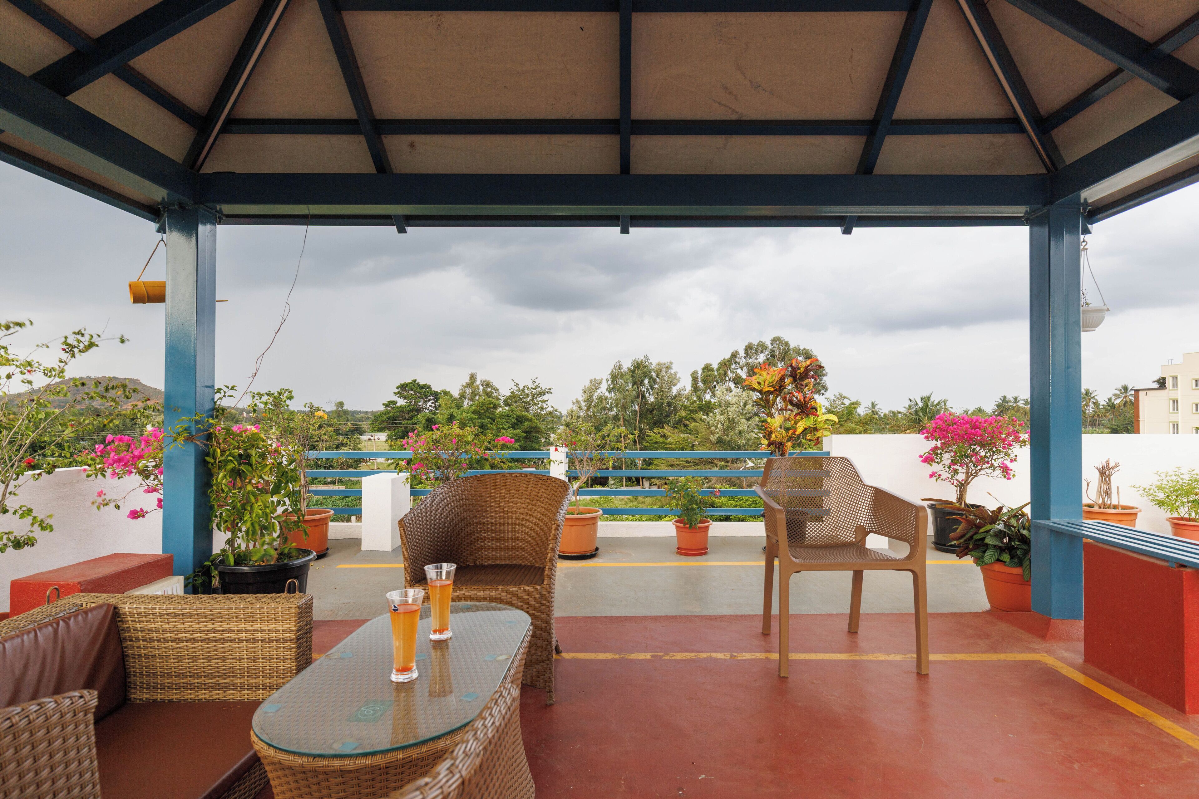 An outdoor seating area with wicker furniture, a glass-top table, and potted plants.