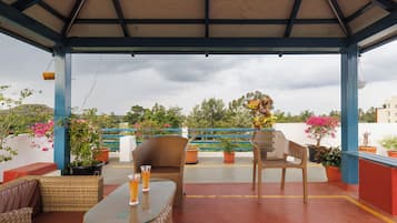 An outdoor seating area with wicker furniture, a glass-top table, and potted plants.