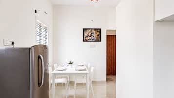 A modern kitchen with a stainless steel refrigerator, white dining table with chairs, and a ceiling fan.
