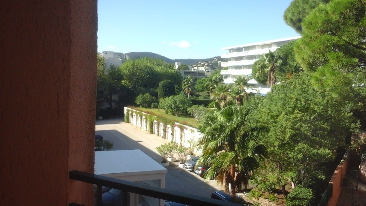 Un balcon donnant sur un immeuble, de la verdure et des voitures garées.
