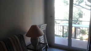 Ein Zimmer mit einer Couch, einem Tisch mit Lampe und einer Schiebeglastür, die auf einen Balkon im Freien führt.
