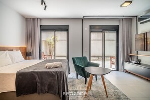 A modern hotel room with a bed, a green armchair, a small table, a TV, and a sliding glass door leading to an outdoor area. - Studio 800m From Beira-mar Norte Ech0106 (Florianópolis)