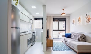 A modern apartment with a kitchenette, a living area with a sofa and artwork, and a large window with curtains. - Complete Studio in Floripa Downtown Ech0205 (Florianópolis)
