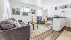 A modern living room with a grey sofa, a small coffee table, and a kitchen area with a bar counter. - Coffield - Comfort, Privacy, and Convenience in Killeen, Texas (Killeen)