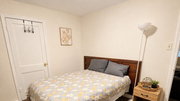 A bedroom with a bed, a nightstand, a lamp, a door, and a wall-mounted picture. - Coffield - Comfort, Privacy, and Convenience in Killeen, Texas (Killeen)