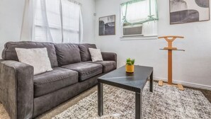 A living room with a grey sofa, a coffee table, a small plant, and a wooden cat tree. - Coffield - Comfort, Privacy, and Convenience in Killeen, Texas (Killeen)