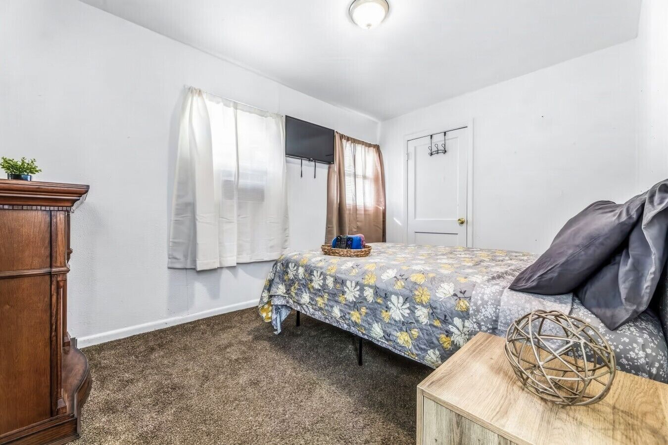 A bedroom with a bed, a wooden dresser, a door, and a small table with a decorative item.