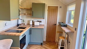 A compact kitchen with a wooden countertop, a built-in oven, and a window with a view of greenery. - Peaceful Shepherd Hut Near Clovelly (Bideford)
