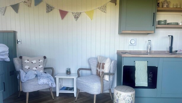 A cozy room with a kitchenette, two armchairs, a small table, and a decorative bunting. - Peaceful Shepherd Hut Near Clovelly (Bideford)