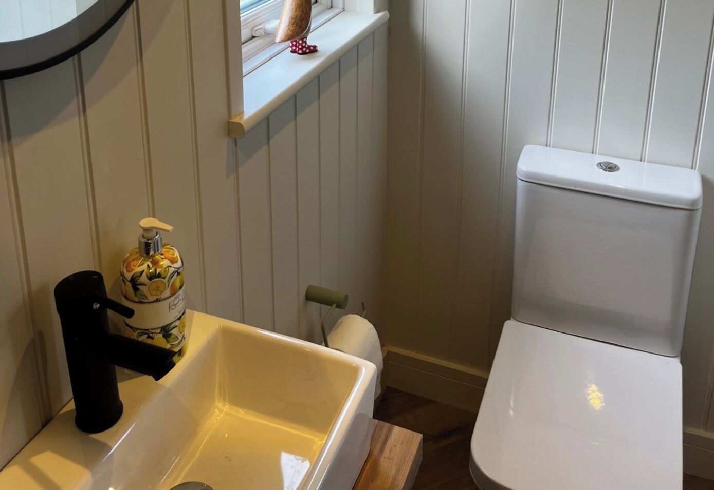 Ein Badezimmer mit Toilette, Waschbecken, einem Fenster mit Dekoration und einem Toilettenpapierhalter.