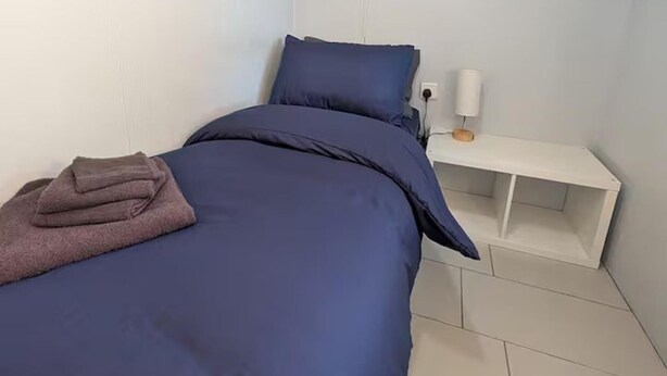 A bedroom with a bed, a bedside table, and a wall-mounted cabinet.