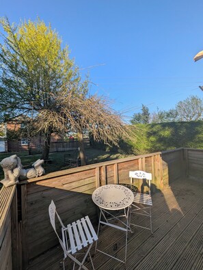 A wooden deck with two white metal chairs and a small round table. - Fish Shack at Rampart - Rustic Stay (Spalding)