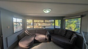 A room with a sectional sofa, large windows with blinds, a ceiling light, and a tiled floor.