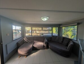 A room with a sectional sofa, large windows with blinds, a ceiling light, and a tiled floor. - Fish Shack at Rampart - Rustic Stay (Spalding)