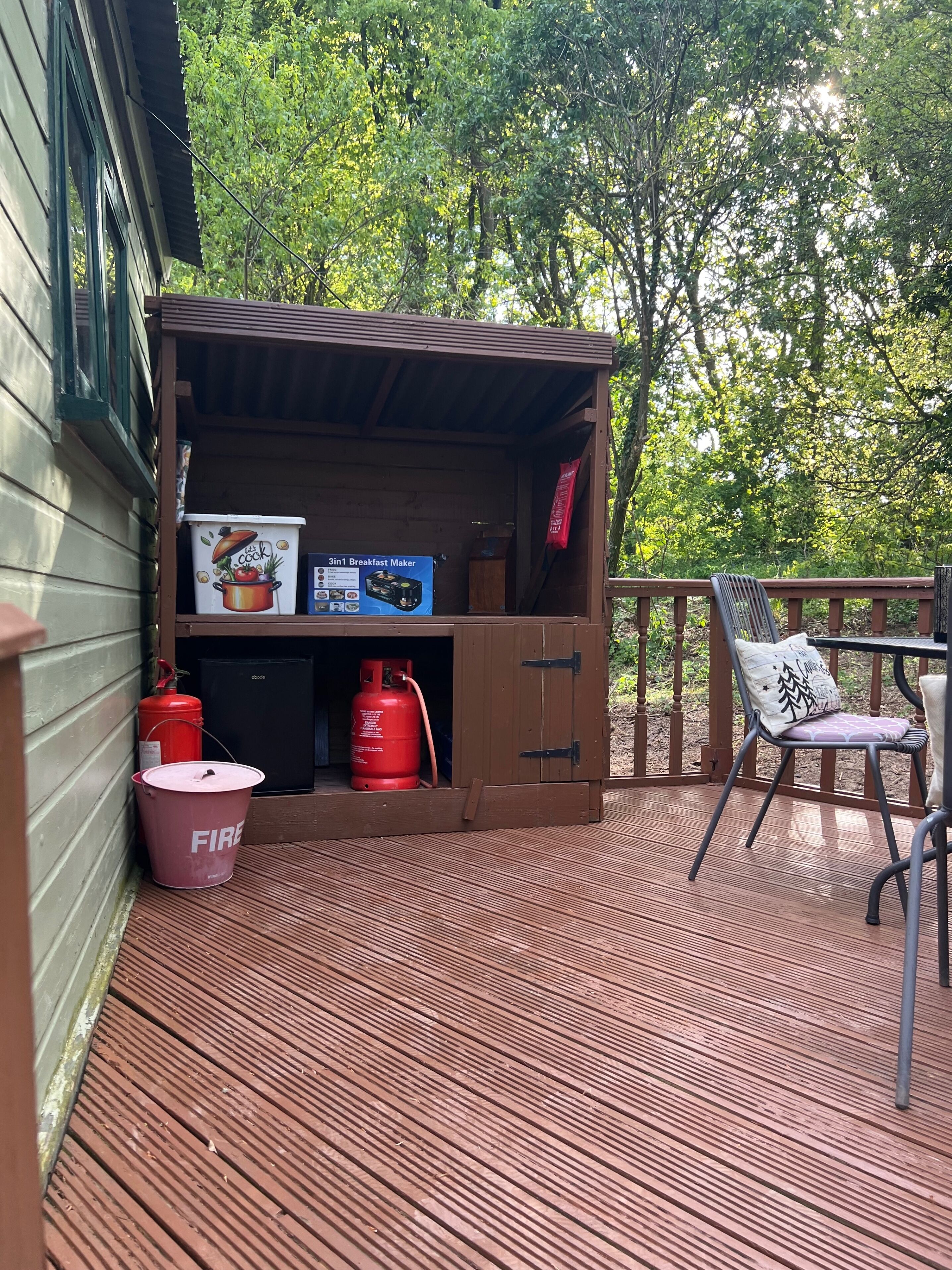 A wooden deck with a small kitchenette area, a fire extinguisher, and a chair.