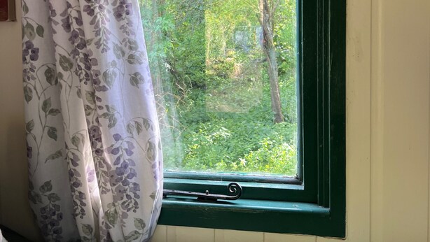 A bedroom with a window, a bed, and a curtain. - Fern Cosy Woodland Shepherds Hut Walk to Sea (Holyhead)