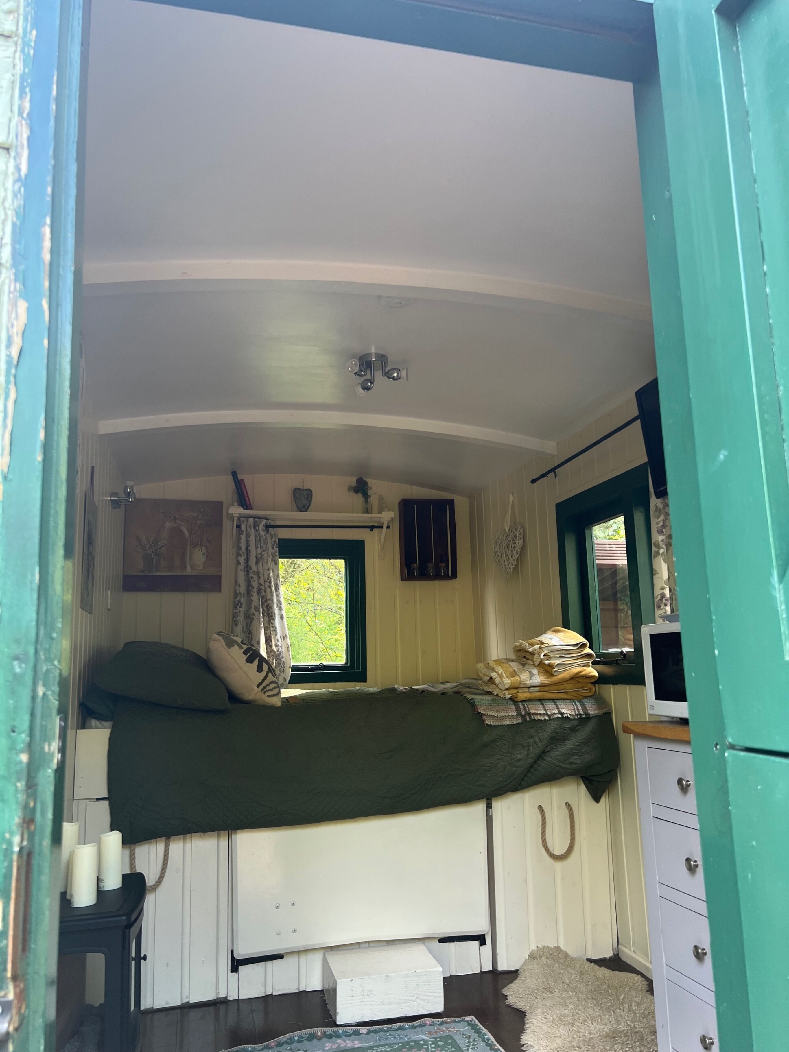 Una habitación pequeña y acogedora con una cama individual, una ventana con cortinas, una mesita con velas y un aparador.