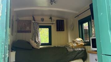 Una habitación pequeña y acogedora con una cama individual, una ventana con cortinas, una mesita con velas y un aparador.