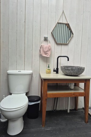 A bathroom with a white toilet, a wooden sink with a stone basin, a hanging towel, and a mirror.