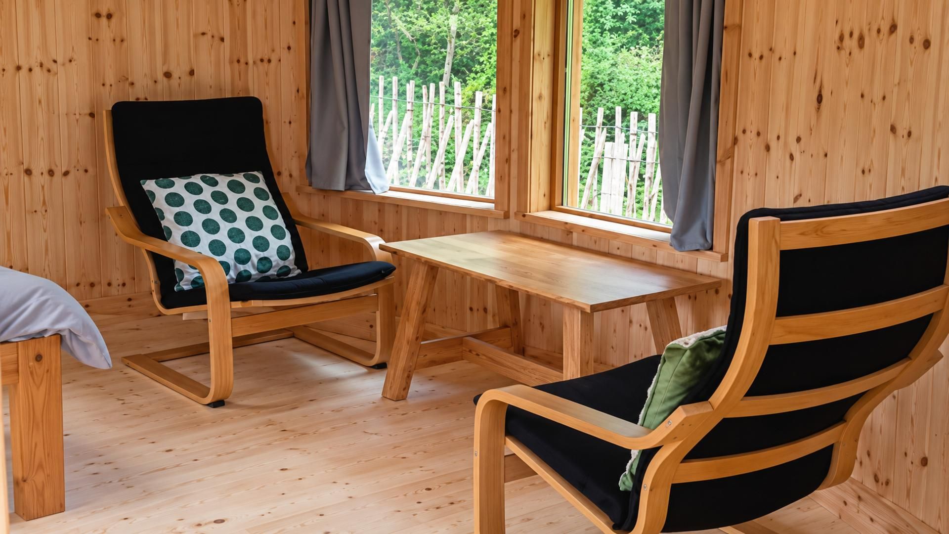 A wooden room with two chairs, a small table, and a window with curtains.