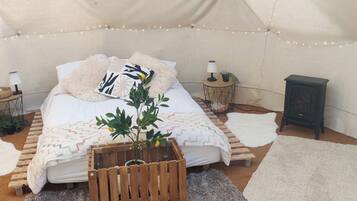 Una habitación con tienda de campaña acogedora, con cama, una mesita con lámpara, un calentador y una planta.