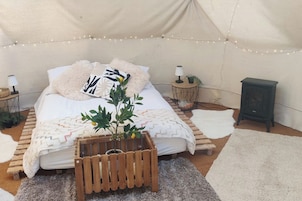 Una habitación con tienda de campaña acogedora, con cama, una mesita con lámpara, un calentador y una planta.