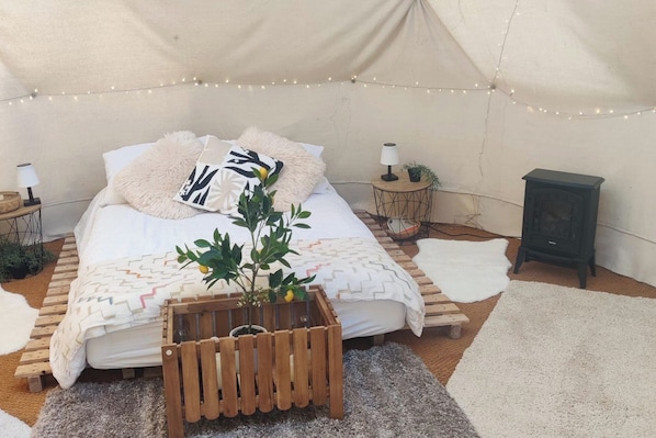 A cozy tented room with a bed, a small table with a lamp, a heater, and a plant.