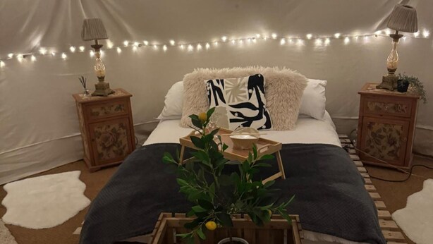 A cozy bedroom with a bed, two nightstands, string lights, a potted plant, and a wooden crate. - Pewsey Countryside Dome - Dog Friendly - Fire pit (Pewsey)