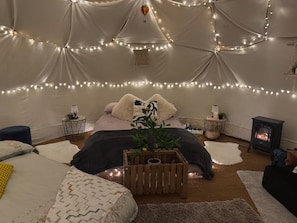 A cozy tent-style room with a bed, bedside tables, a small heater, string lights, and a potted plant. - Pewsey Countryside Dome - Dog Friendly - Fire pit (Pewsey)