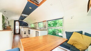 Cocina compacta con una isla central, comedor con mesa de madera y sofá con cojines.