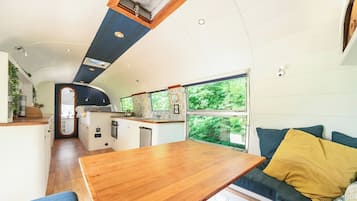 A compact kitchen with a central island, a dining area with a wooden table, and a sofa with cushions.